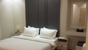 A modern bedroom with a large bed, bedside tables, a dresser, and a mirror. - alfursan servived appartment (Al Kharj)
