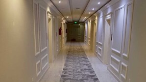 A hotel hallway with patterned carpet, white walls, and doors on both sides. - alfursan servived appartment (Al Kharj)