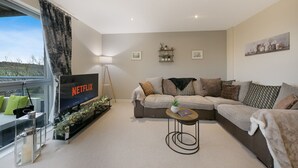 Un salon avec un téléviseur, un canapé, une table basse et une fenêtre avec des rideaux.