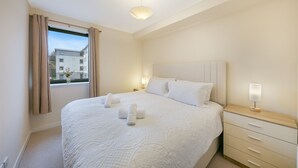 Une chambre d’hôtel avec un grand lit, une table de chevet, une commode et une fenêtre avec des rideaux.