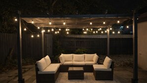Un patio al aire libre con un sofá modular, una mesa de centro y luces colgantes.