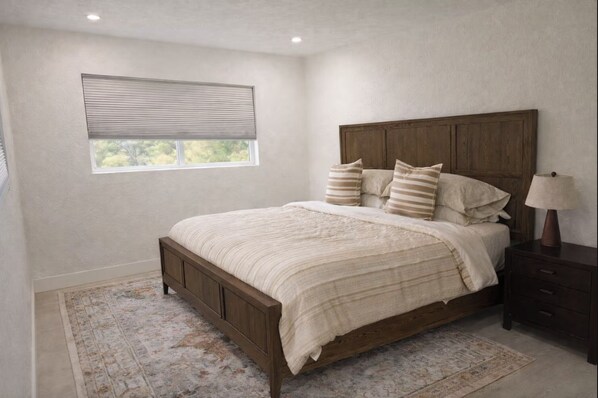 Une chambre à coucher avec un lit en bois, une table de chevet, une lampe, une fenêtre avec des stores et un tapis à motifs.