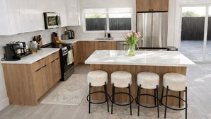 Una cocina moderna con armarios blancos, un refrigerador de acero inoxidable, horno empotrado e isla central con taburetes de bar.