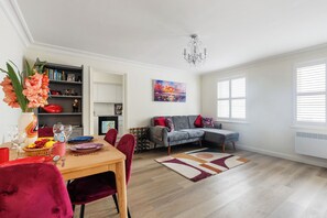Ein modernes Wohnzimmer mit Essbereich, ausgestattet mit einem grauen Sofa, roten Sesseln, einem Holzesstisch und einer Chandelier.