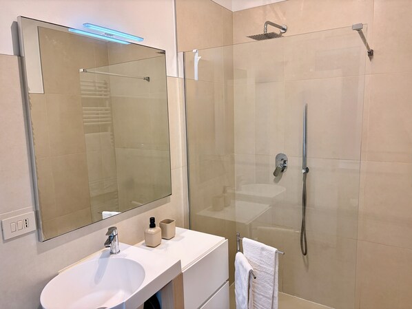 A modern bathroom with a glass-enclosed shower, a white sink, and a large mirror. - Smile (Venice)