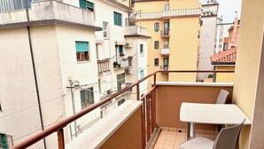 Ein Balkon mit weißem Tisch und Stuhl, Geländer und Blick auf benachbarte Gebäude.