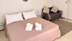 Ein ordentlich bezogenes Bett mit einer rosafarbenen Steude, zwei weißen Kissen und zwei gerollten weißen Handtüchern.