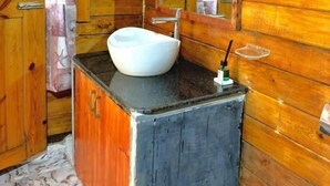 Un baño de cabaña de madera con un lavamanos blanco, un espejo y una cortina de ducha.