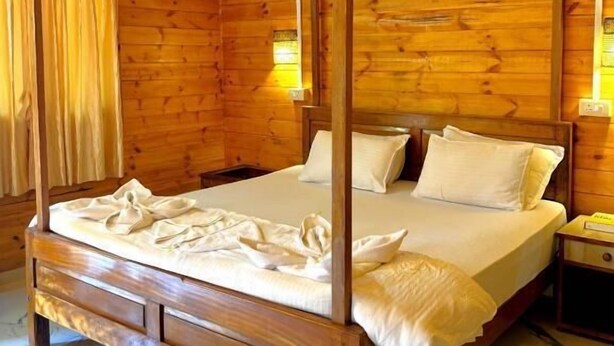 Una cama con dosel en una habitación tipo cabaña de madera, con ventilador de techo, paredes de madera y suelo de mármol.
