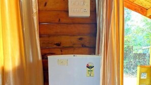 Habitación compacta con pared de madera, una mesita con refrigerador blanco y vistas a espacios verdes.