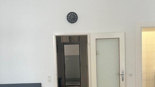 A room with a bed, a door leading to a hallway, and a clock on the wall. - Modern 1BR City Apt for 5 Great Location (Vienna)