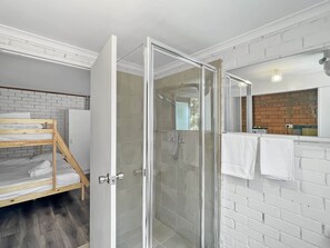 A modern bathroom with a glass-enclosed shower, a wooden bunk bed, and a white brick wall. - Family Beach House with Outdoor Entertaining (Long Beach)