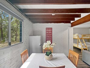 A cozy room with a white brick wall, a wooden ceiling, a white table with chairs, a refrigerator, and a bunk bed. - Family Beach House with Outdoor Entertaining (Long Beach)