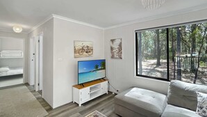 Uma sala de estar moderna com televisão, sofá, janela com vista para uma floresta e uma obra de arte com tema de bicicleta.