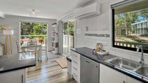 Cozinha moderna com uma janela grande, armários brancos e uma área de jantar com vista para o exterior.
