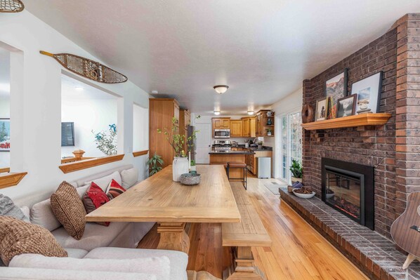 A modern kitchen with a large wooden table, a brick fireplace, and wooden cabinets. - All king beds (with 2 rooms that can convert into 2 twin XLs), hot tub, arcade, and fresh updates. Spacious, cozy, and minutes to Snowbird & Alta. Pet-friendly and perfect for ski groups wanting comfort, style, and unbeatable canyon access. (Sandy)