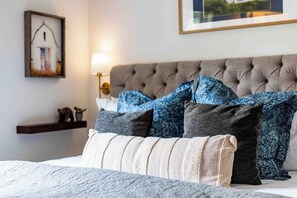 A neatly made bed with a grey tufted headboard, multiple pillows in shades of blue and grey, a small shelf with decorative items, and a framed picture on the wall. - All king beds (with 2 rooms that can convert into 2 twin XLs), hot tub, arcade, and fresh updates. Spacious, cozy, and minutes to Snowbird & Alta. Pet-friendly and perfect for ski groups wanting comfort, style, and unbeatable canyon access. (Sandy)