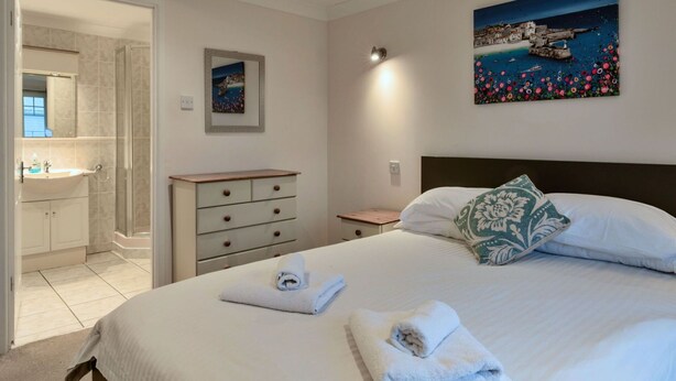 Een slaapkamer met een bed, nachtkastje, kaptafel, schilderij en een badkamer die door een open deur zichtbaar is.