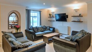 Een moderne woonkamer met een zithoek, een salontafel en een flatscreen televisie aan de muur.