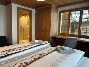 A bedroom with a bed, a window with a view of trees, and a wooden wardrobe. - Serene and relaxing 2 bedroom apartment with panoramic views (Saanen)