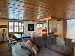 A modern living room with a sofa, chairs, a dining table, and a kitchen area. - Serene and relaxing 2 bedroom apartment with panoramic views (Saanen)