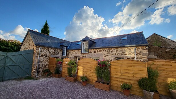 Een stenen huis met een schuin dak, houten poorten en bloempotten.