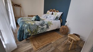 Een slaapkamer met een bed, een geweven vloerkleed, een houten kruk en een wandlamp.