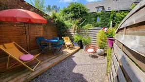 Een houten terras met een tafel, stoelen, een rode parasol en een gele lounge stoel.