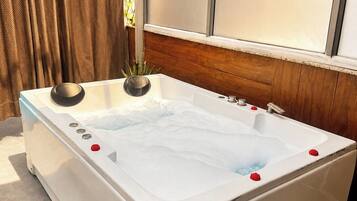 A spa tub with rose petals, a control panel, and a window with curtains.