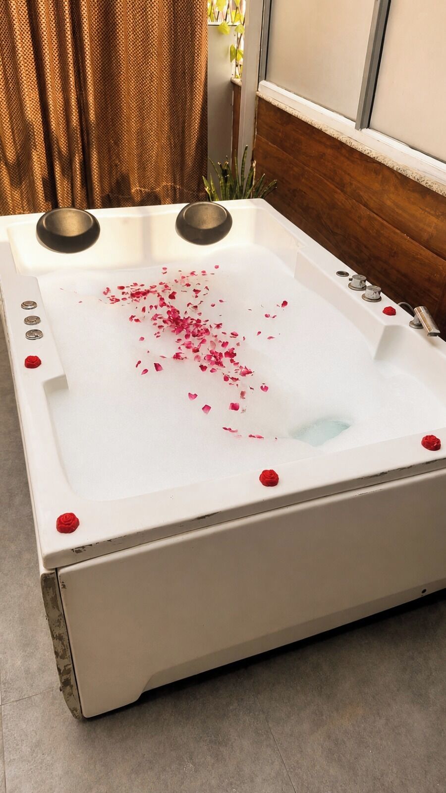 A white bathtub with rose petals and a single red rose on the edge.