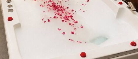 A white bathtub with rose petals and a single red rose on the edge.