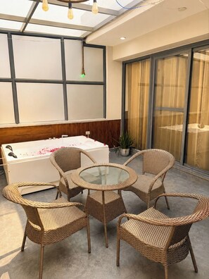Une pièce comprenant une table ronde au plateau en verre, entourée de chaises en osier, un canapé blanc et une grande fenêtre offrant une vue dégagée.
