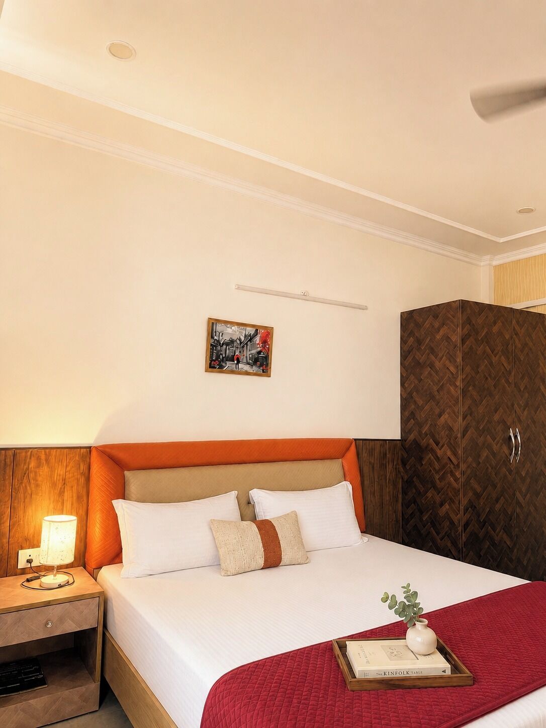A hotel room with a bed, a nightstand, a lamp, a painting, and a wardrobe.