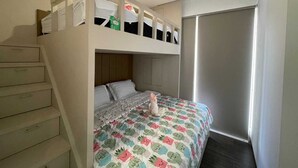 A bunk bed room with a built-in desk and drawers, a closet, and a window.