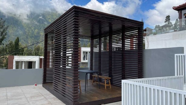 A modern outdoor patio with a wooden pergola structure, a dining table, and a view of the surrounding landscape.
