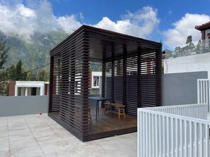 A modern outdoor patio with a wooden pergola structure, a dining table, and a view of the surrounding landscape. - Orlando Hill Villa (Ngadisari)