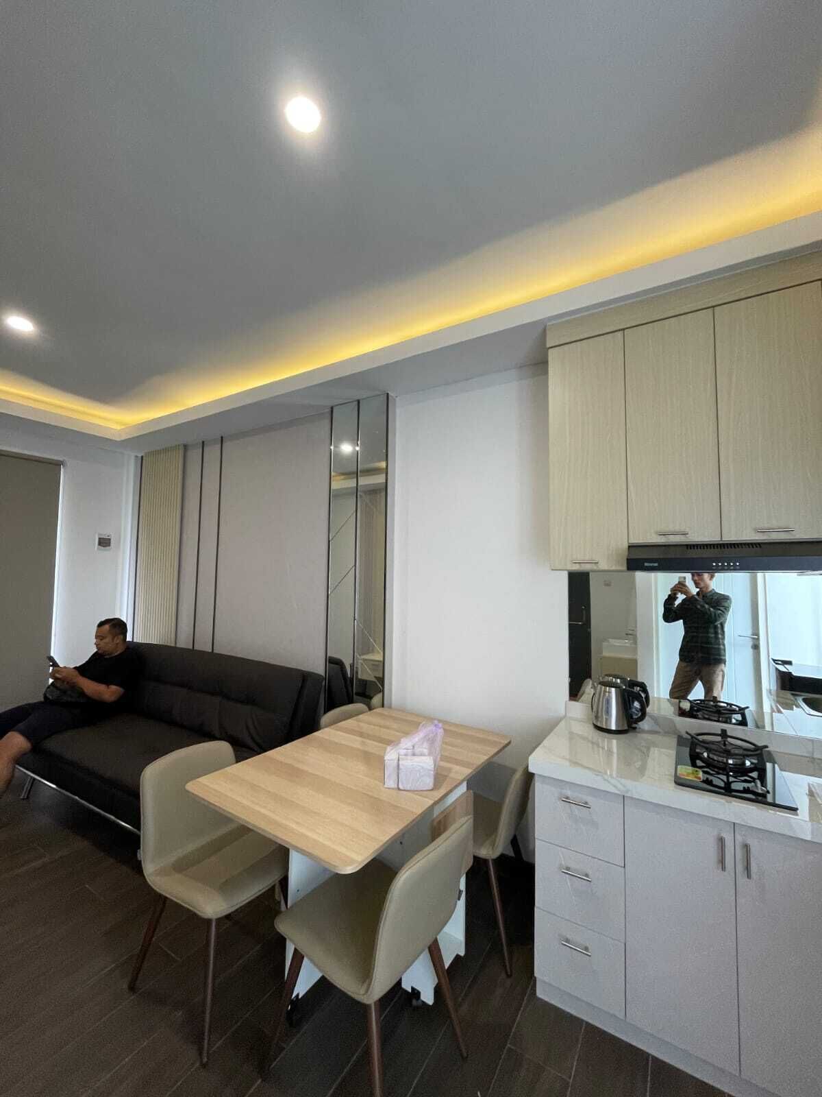 A modern living room with a sofa, a dining table with chairs, a kitchen area with cabinets and a stove, and a large mirror.