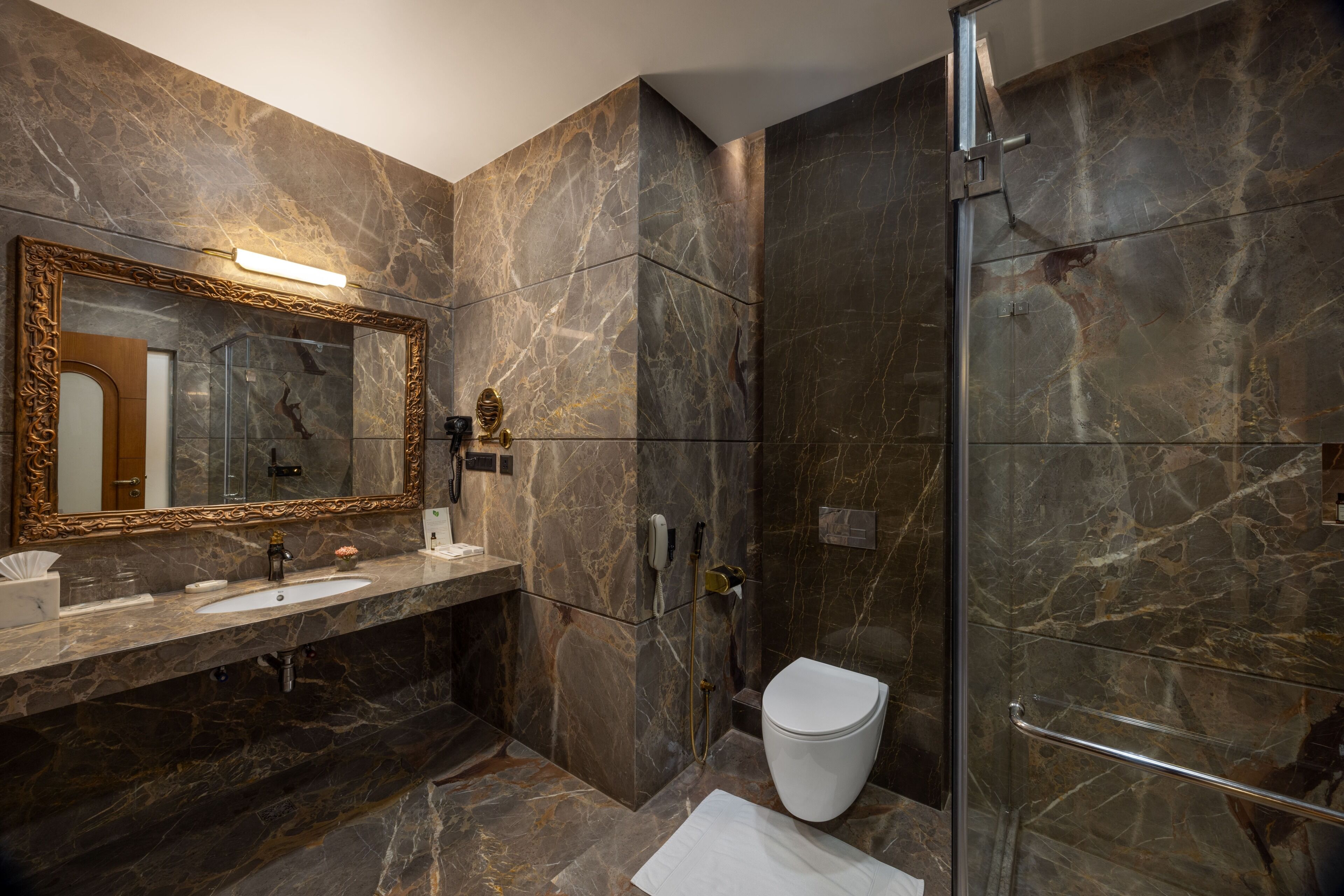 Ein Badezimmer mit Marmorwaschbecken, Toilette, Dusche und einem großen Spiegel.