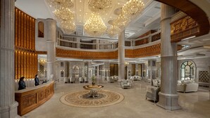 Un vaste hall d’entrée avec de hauts plafonds, de somptueux lustres et une grande table ronde au centre.