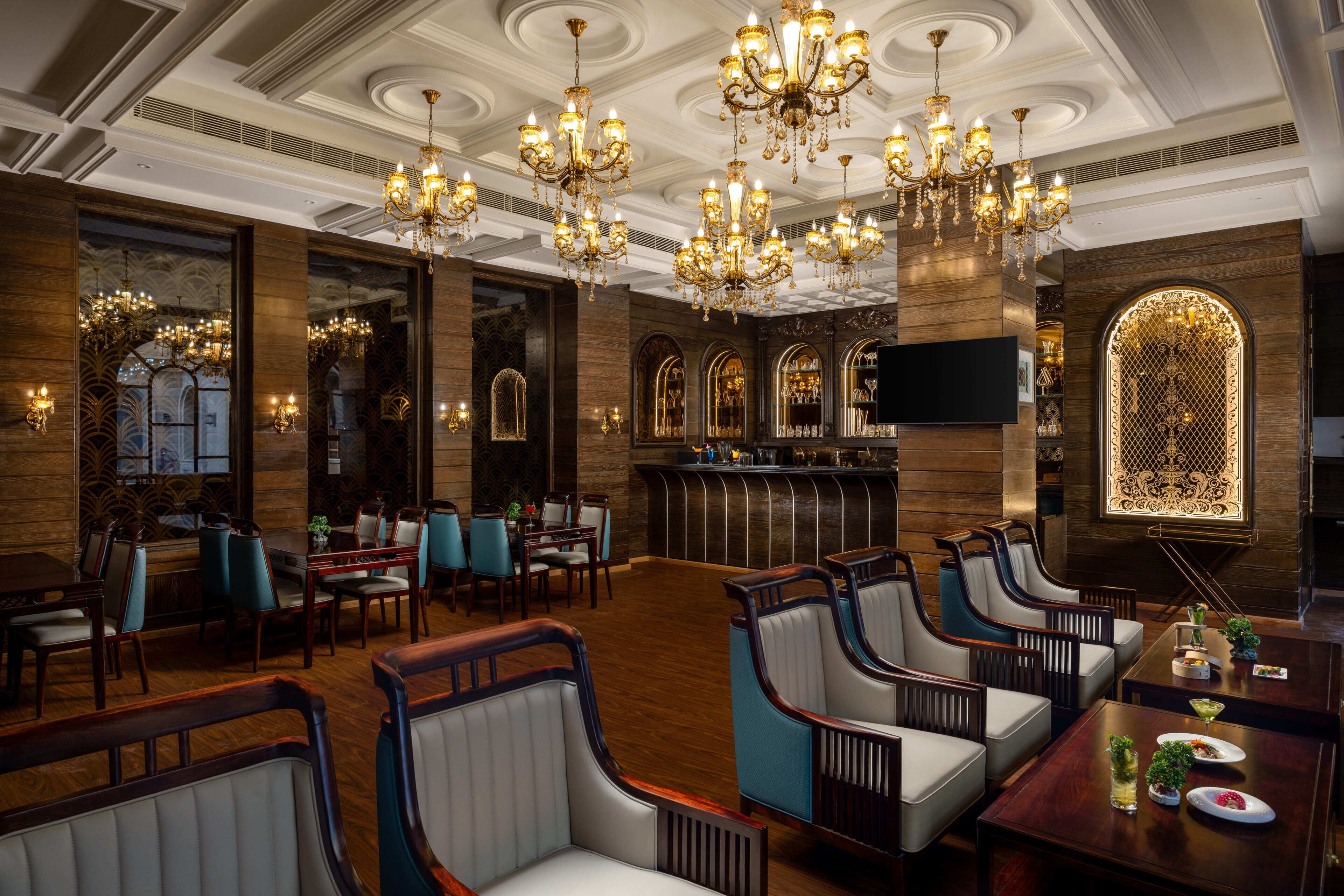 A spacious hotel lobby with ornate chandeliers, wooden paneling, and a bar area.
