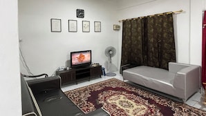 Una sala de estar con un sofá, un televisor, un ventilador y un tapete estampado.