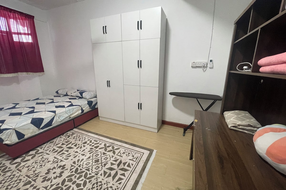 Ein Schlafzimmer mit Bett, Kleiderschrank, einem kleinen Tisch und einem Regal mit Handtüchern.
