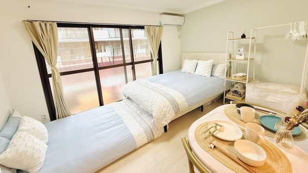 Ein Zimmer mit zwei Betten, einem Esstisch mit Tellern und Tassen sowie einem Fenster mit Vorhängen.