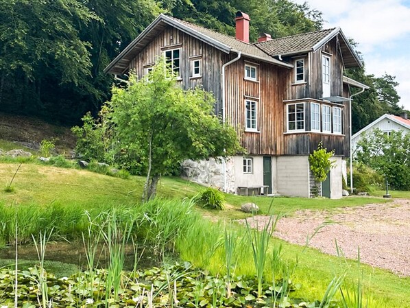 A two-story wooden house with a sloped roof, surrounded by a grassy area and a small pond. - 4 Star Holiday Home in Uddevalla (Uddevalla)