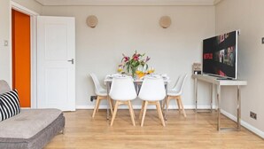 Ein modernes Wohnzimmer mit Essbereich, einer Couch, einem Fernseher und einer Tür, deren Wand in Orange gehalten ist.