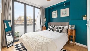 Ein Schlafzimmer mit einem großen Bett, einer Schiebetür zum Balkon, tealfarbenen Wänden und einem Holzboden.