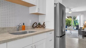 Una cocina moderna con armarios blancos, un lavamanos de acero inoxidable y un refrigerador.