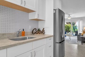 A modern kitchen with white cabinets, a stainless steel sink, and a refrigerator. - Sandy Toes Retreat (Panama City Beach)