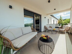A modern balcony with a sofa, wicker chairs, a round table with fruit, and a glass door leading to a room. - Villa Budimir by Interhome (Imotski)