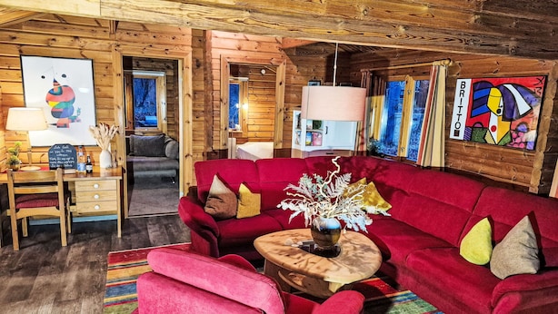 Ein gemütliches Blockhaus-Interieur mit einem roten Sofa, einem Holztisch und einem farbenfrohen Streifen Teppich.